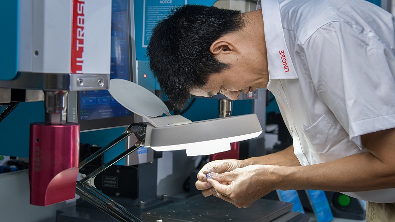 穿白工作服男子借助台灯查看手中物件